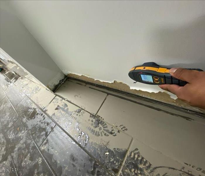 Techs using moisture sensor on drywall in a flood-damaged room